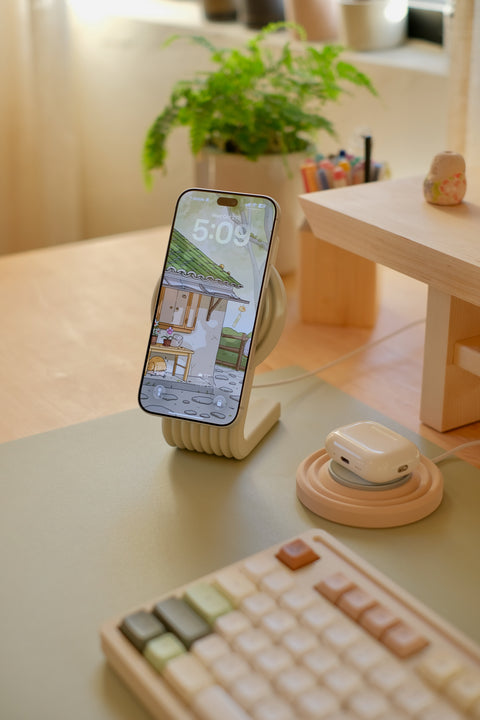 Zen MagSafe Charger Stand in Beige holding an iPhone while it charges, with AirPods on the Charger Puck beside it (puck sold separately)