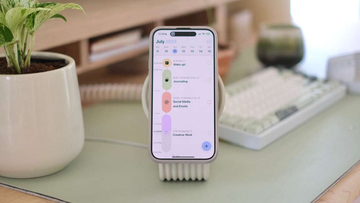 Zen MagSafe Charger Stand holding a phone with the day's plan, next to a plant and keyboard