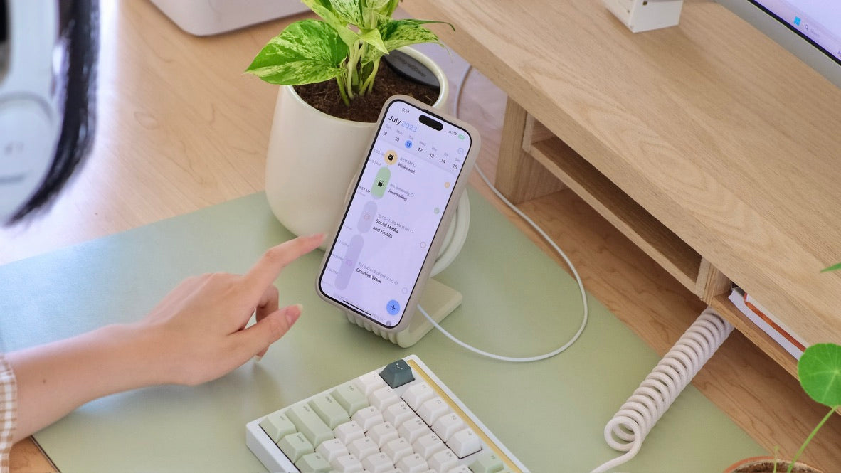 A hand tapping a phone resting on the Zen MagSafe Charger Stand on a Matcha desk mat