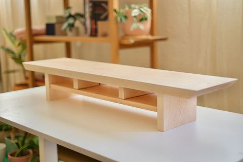 Zen Desk Shelf in Maple, Large (36 in wide), three-quarter view on a white table with the studio bookshelf behind