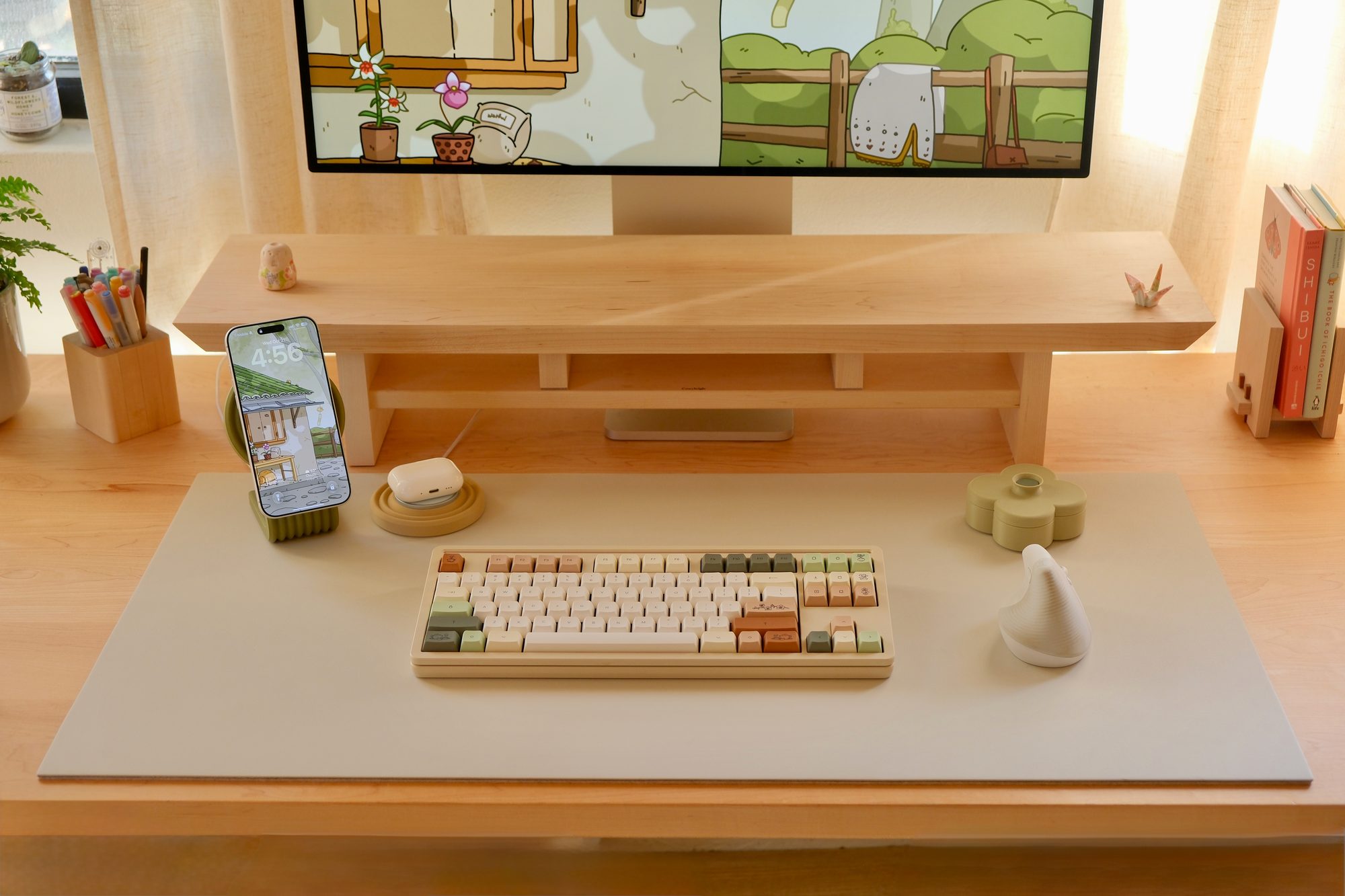 A Beige Cozyleigh Desk Mat with a Moss Zen MagSafe Charger Stand and a Pistachio Fa Trinket Tray, with a phone and AirPods on the stand