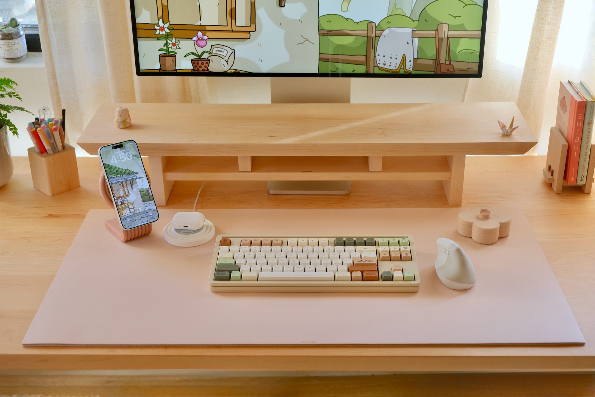 A Blush Cozyleigh Desk Mat with a Rose Zen MagSafe Charger Stand, with a phone and AirPods on the stand