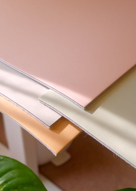 Corners of Cozyleigh Desk Mats in Blush, Matcha and Latte stacked, showing linoleum tops and wool undersides