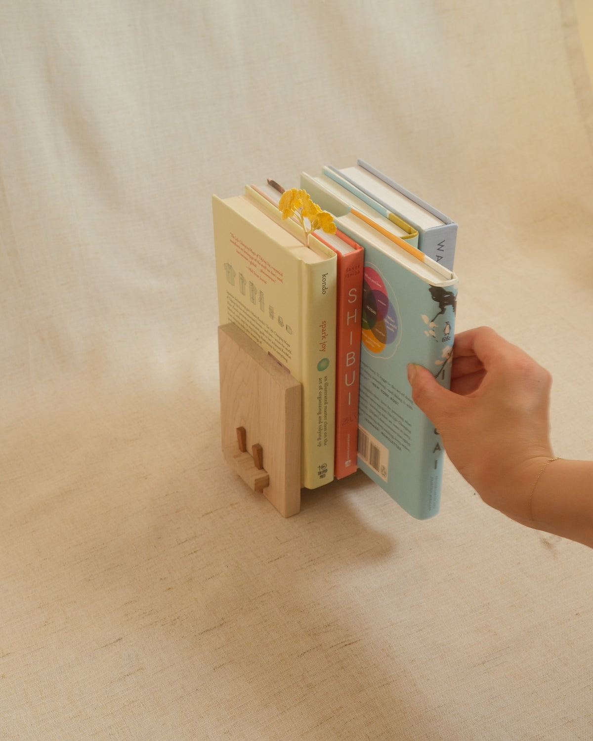 A hand sliding a book out of a Zen Book Stand on linen