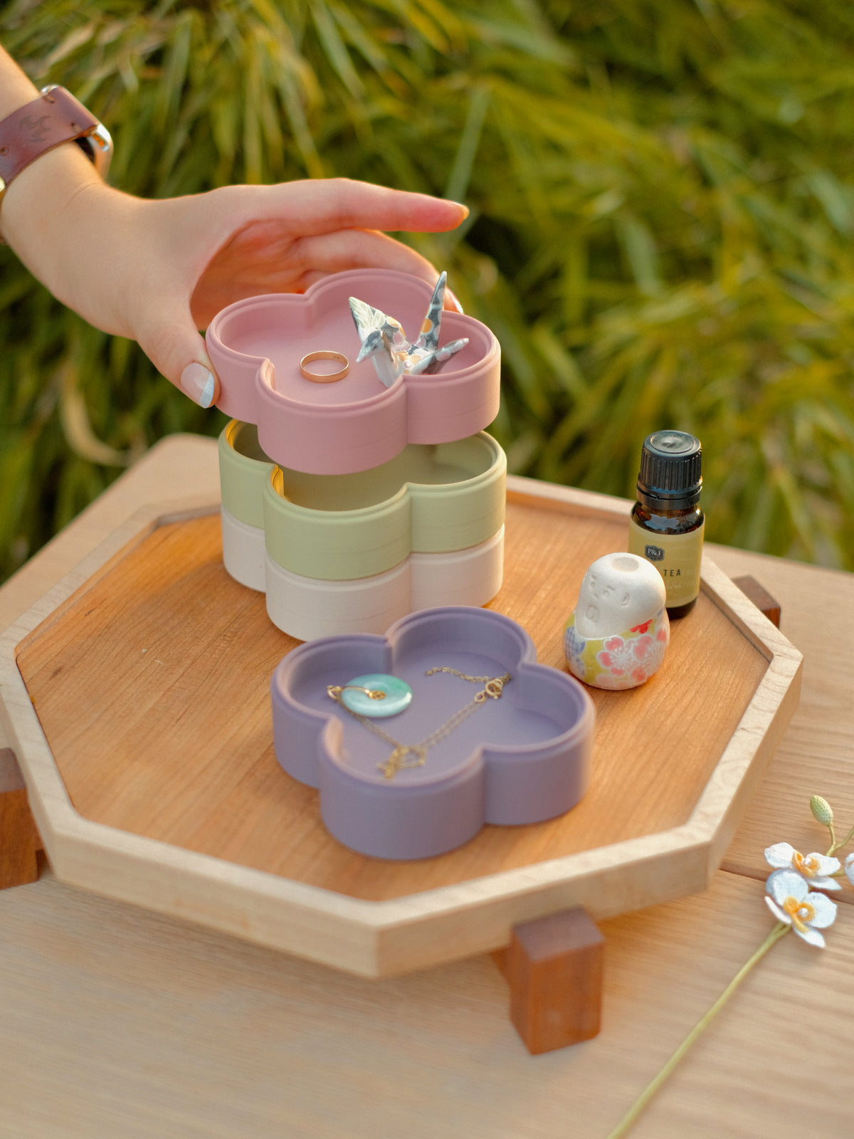 Hand holding a Fa Trinket Tray in Rose with a ring and paper crane above a Pistachio and Dusty Blush stack