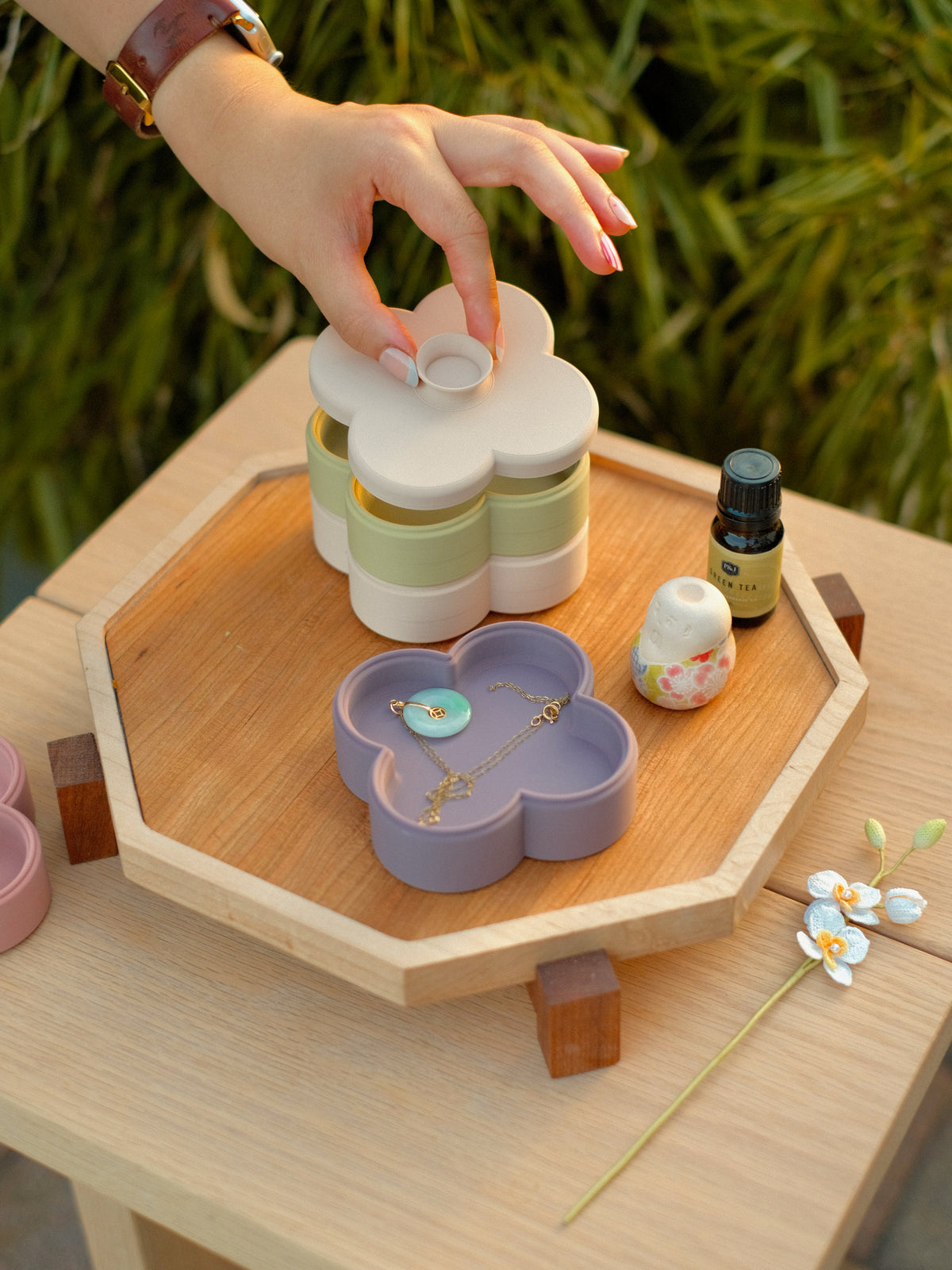 Hand placing the lid on a stack of Fa Trinket Trays, with a lilac tray holding a necklace