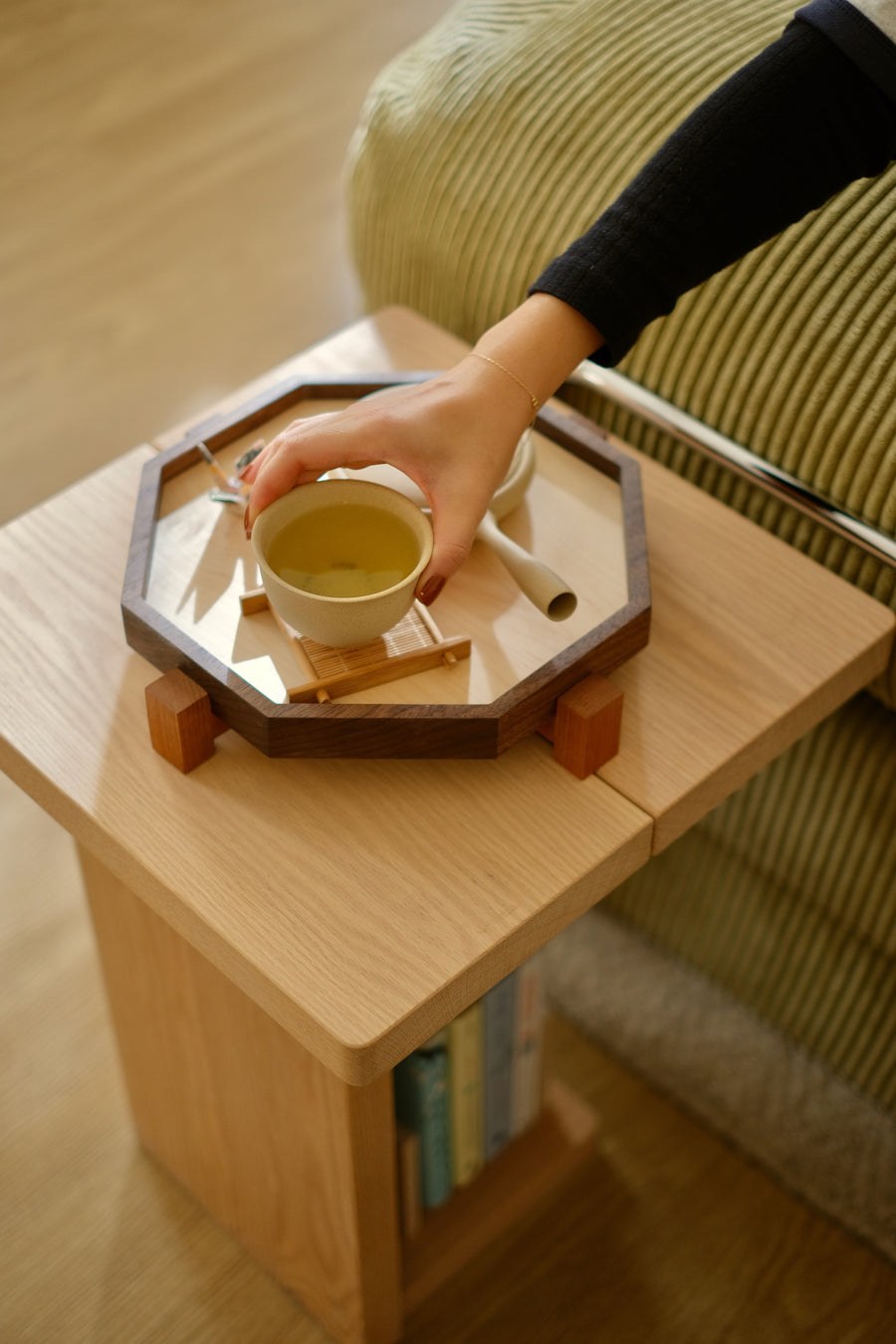 A hand lifting a cup of tea from a walnut Zen Tray on a side table; on computers, the Wood Collection together: a maple Zen Desk Shelf, Zen Tray and Zen Book Stand in front of a linen curtain