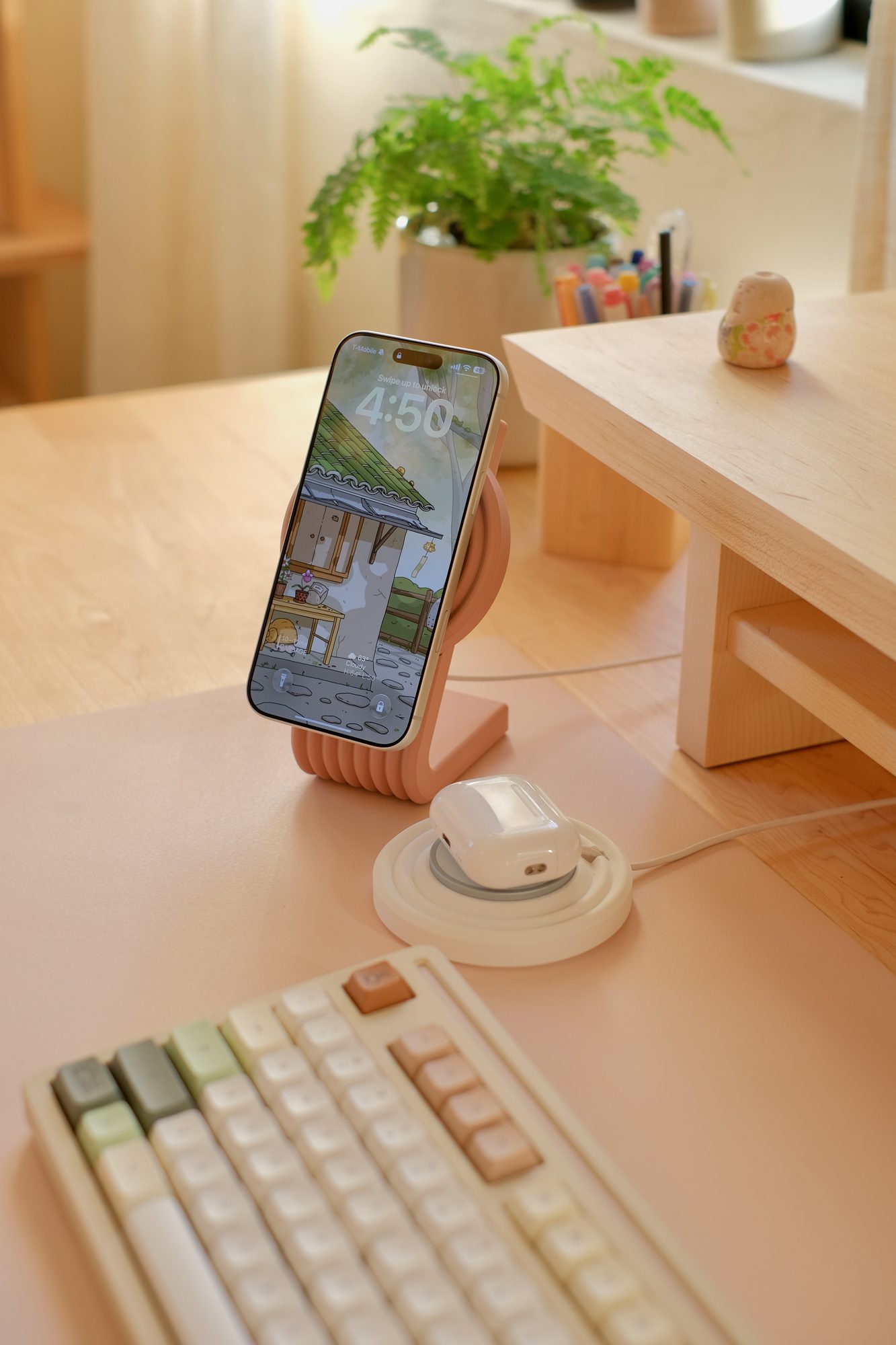A Rose Zen MagSafe Charger Stand holding an iPhone, with AirPods on a White Zen MagSafe Charger Puck, on a Blush Cozyleigh Desk Mat